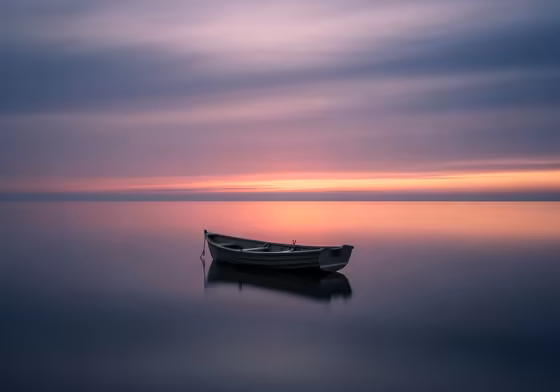 A single, small wooden boat floating on a vast, calm ocean at dusk, symbolizing loneliness and grief.